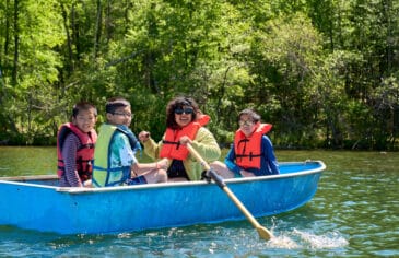 Camp counselor engages with campers while rowing a boat on the camp lake.